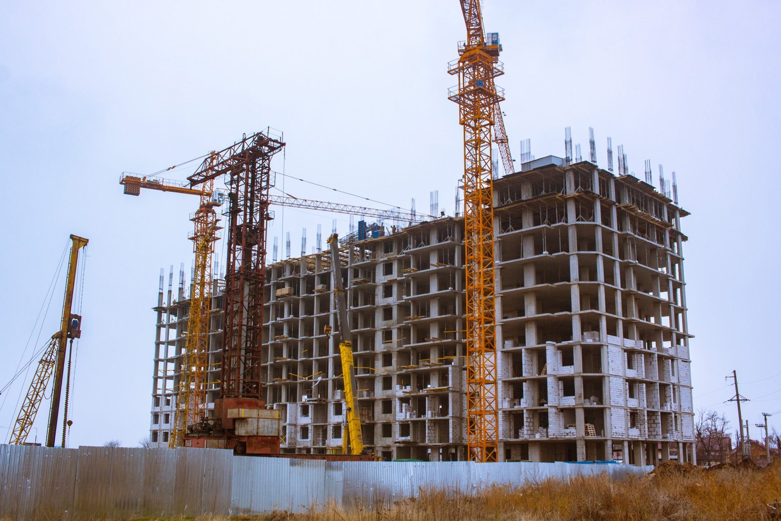 Multi-story reinforced concrete building under construction with tower cranes, exposed structural framework, and active construction site, representing large-scale residential and commercial building development.